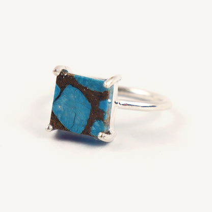Silver ring with a square blue stone on a white background