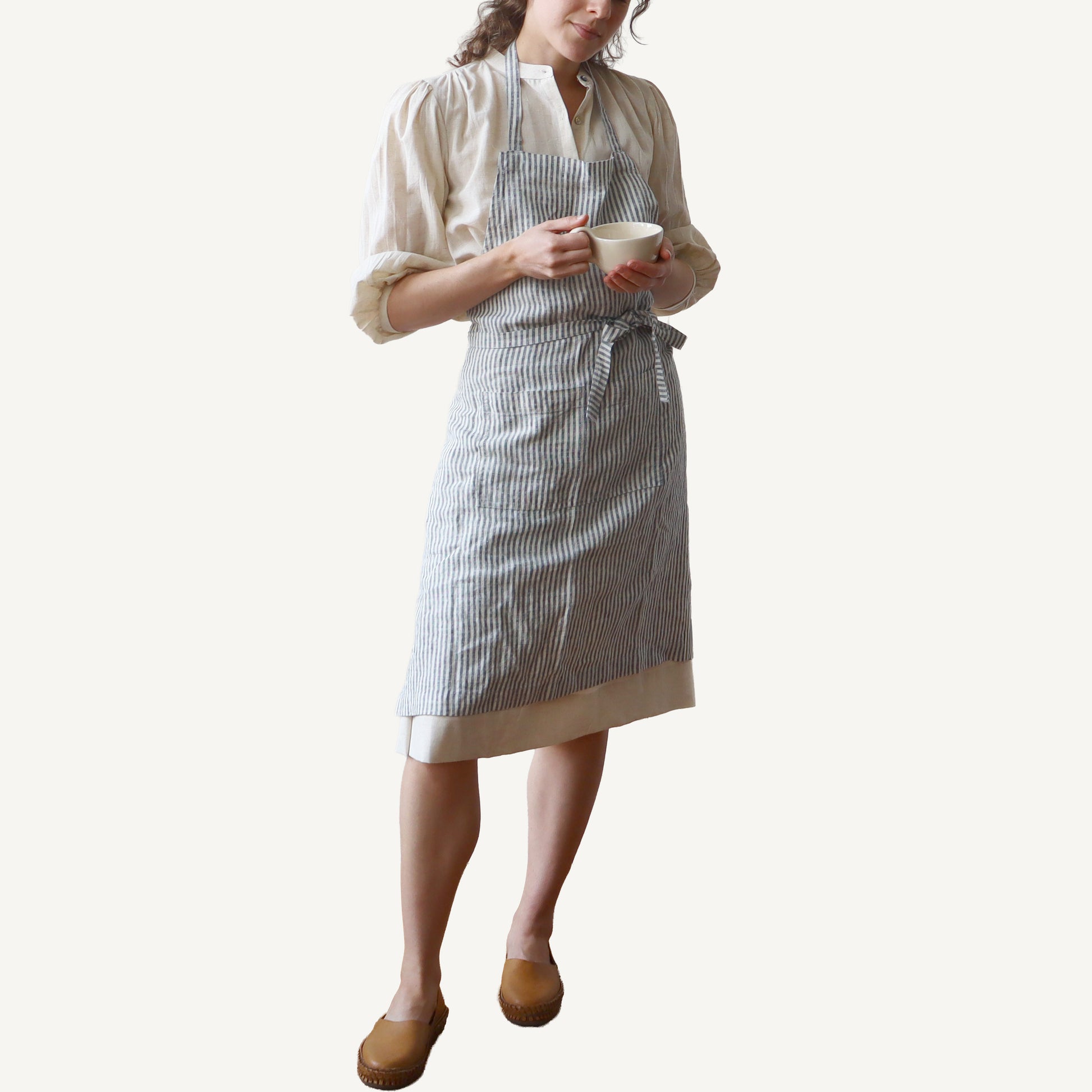Person wearing a striped apron holding a cup on a white background