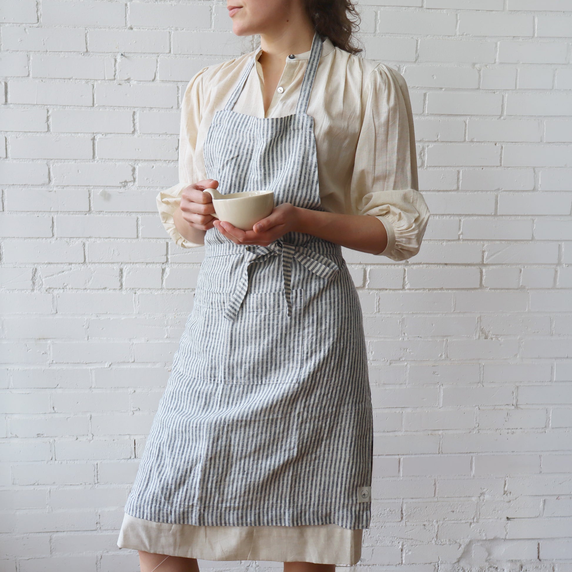 Person wearing a striped apron holding a cup against a white brick wall