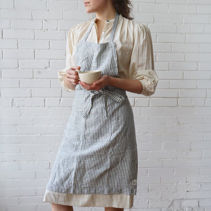 Person wearing a striped apron holding a cup against a white brick wall