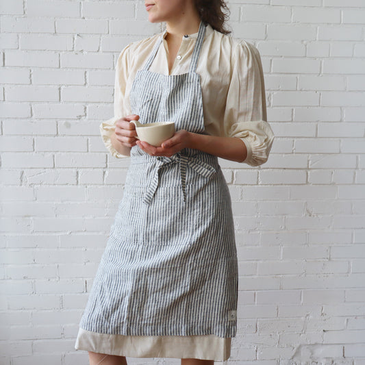 Person wearing a striped apron holding a cup against a white brick wall