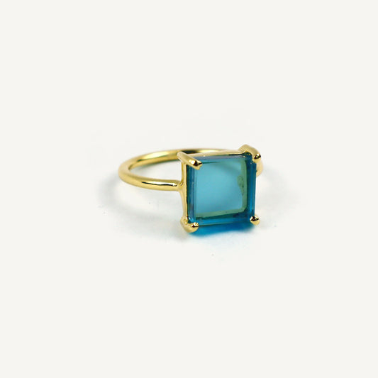 Gold ring with a square blue gemstone on a white background