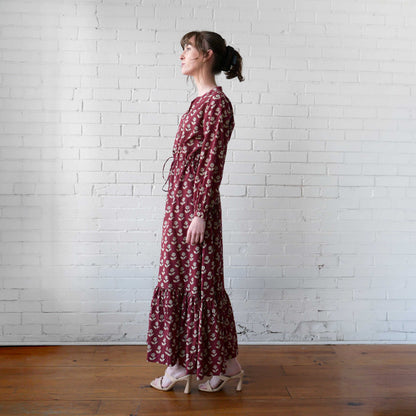 Woman wearing a long floral dress standing against a white brick wall.
