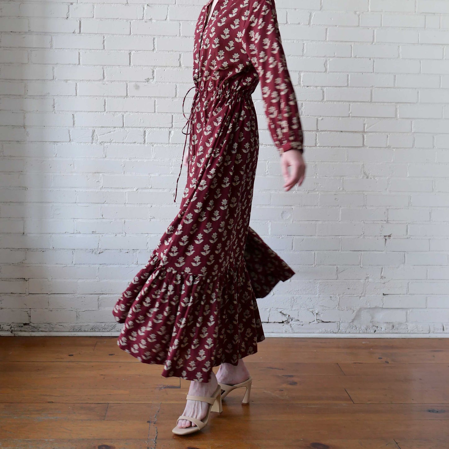 Person wearing a burgundy floral dress against a white brick wall.