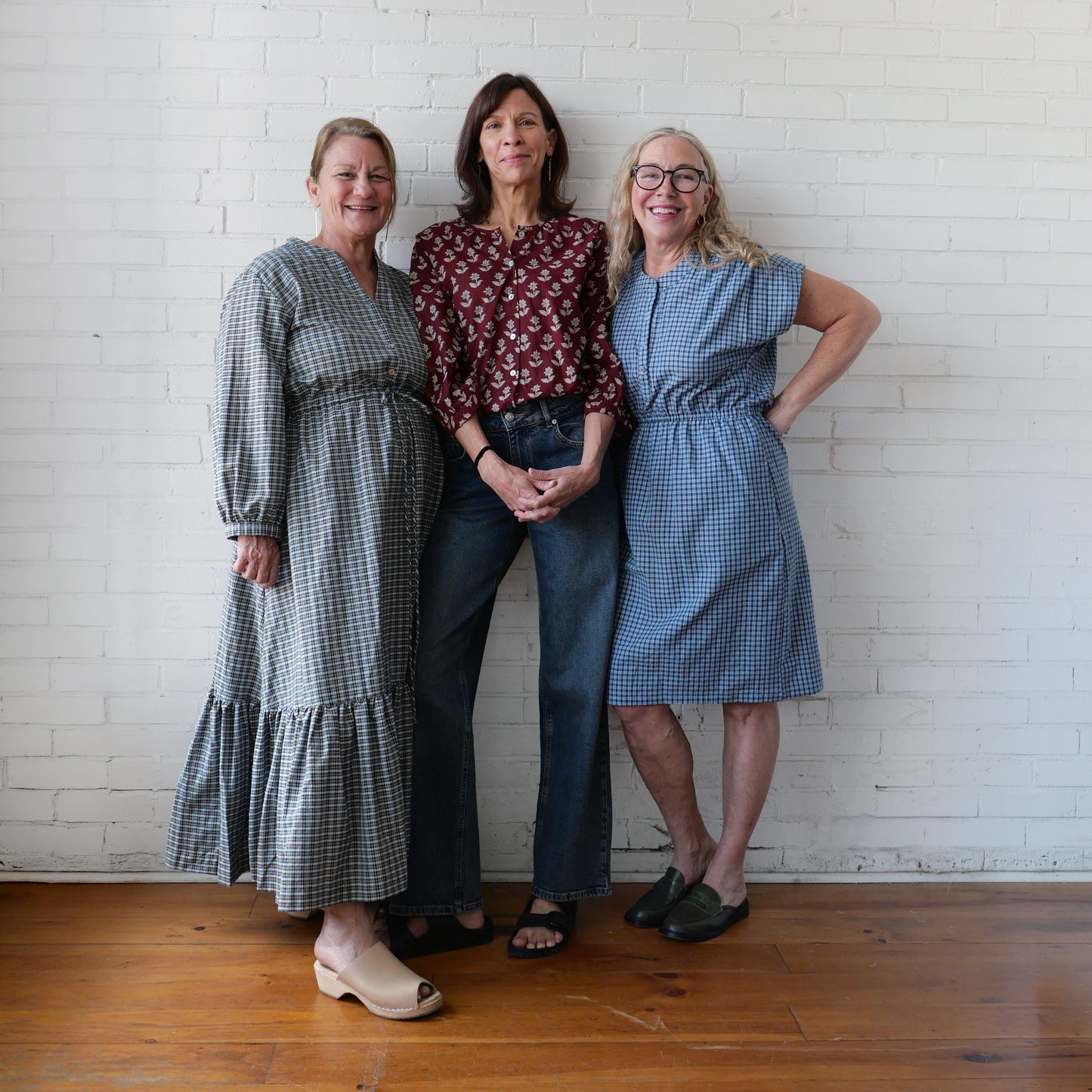 Three women posing together against a white brick wall.