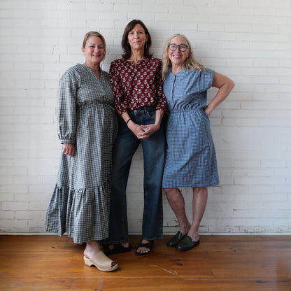 Three women posing together against a white brick wall.