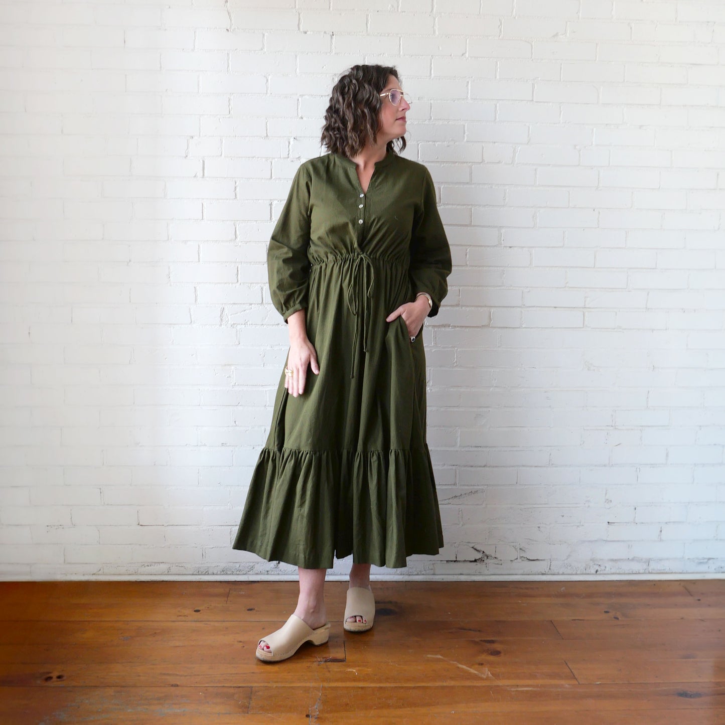 Woman wearing a green dress standing against a white brick wall.