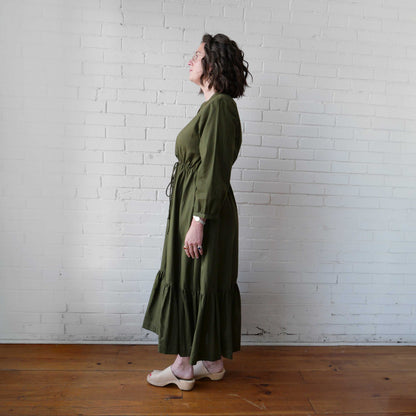 Woman wearing a green dress standing against a white brick wall.