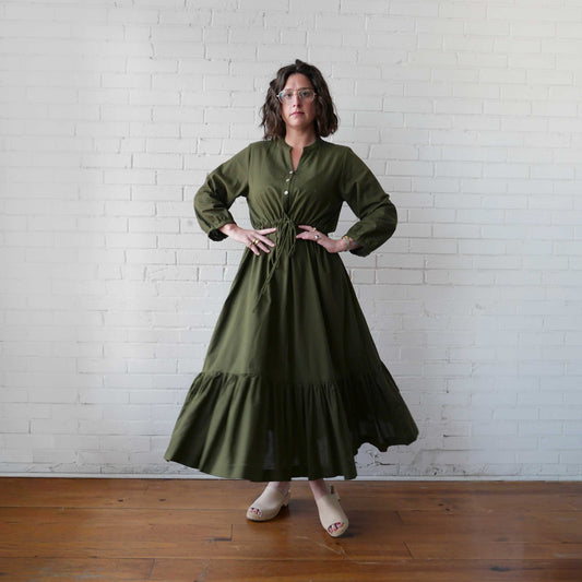 Woman wearing a green dress standing against a white brick wall.