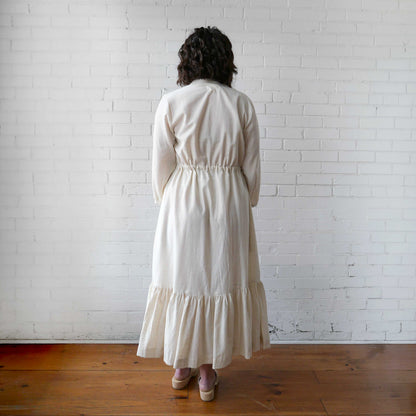 Person wearing a white dress standing against a white brick wall.