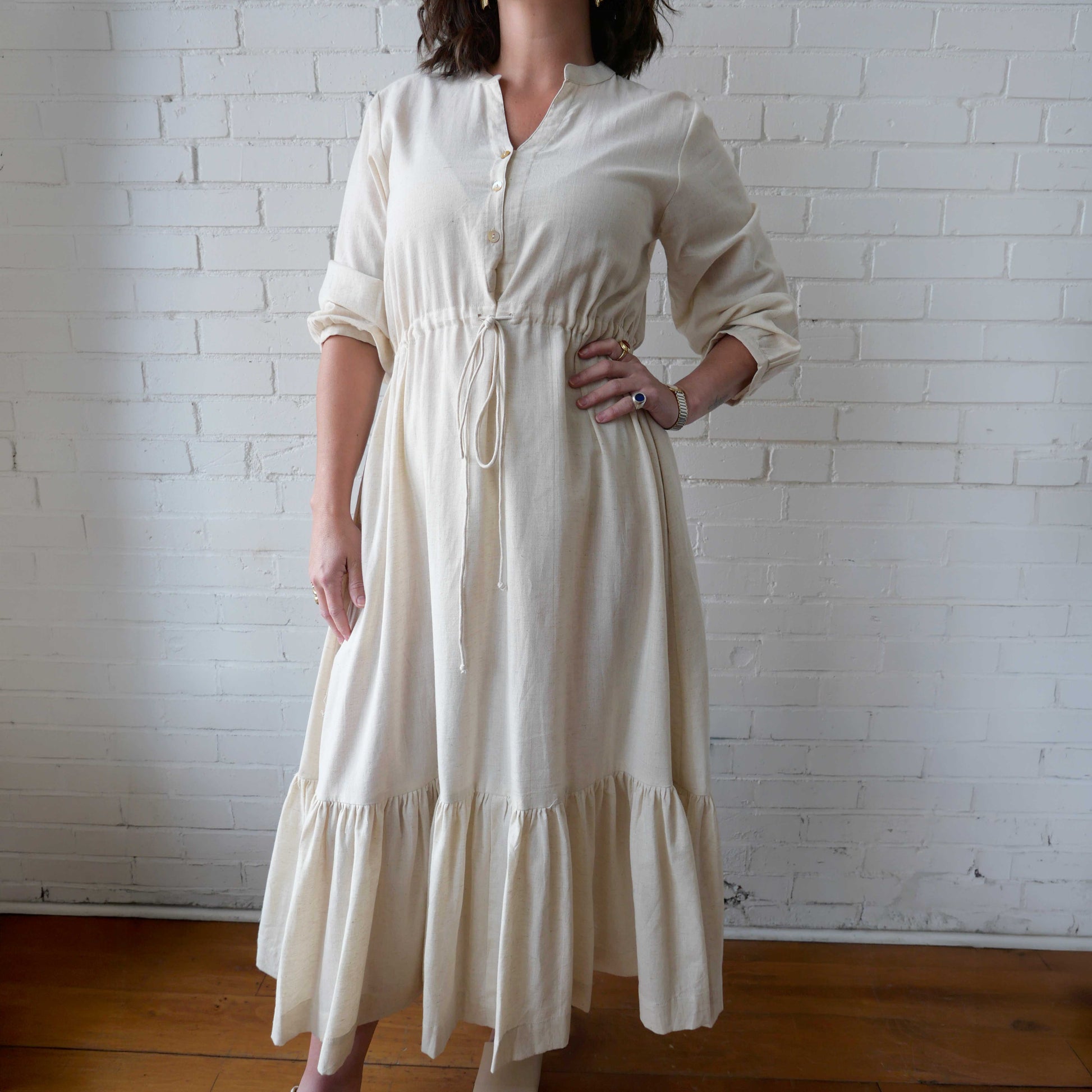 Woman wearing a white dress against a white brick wall.