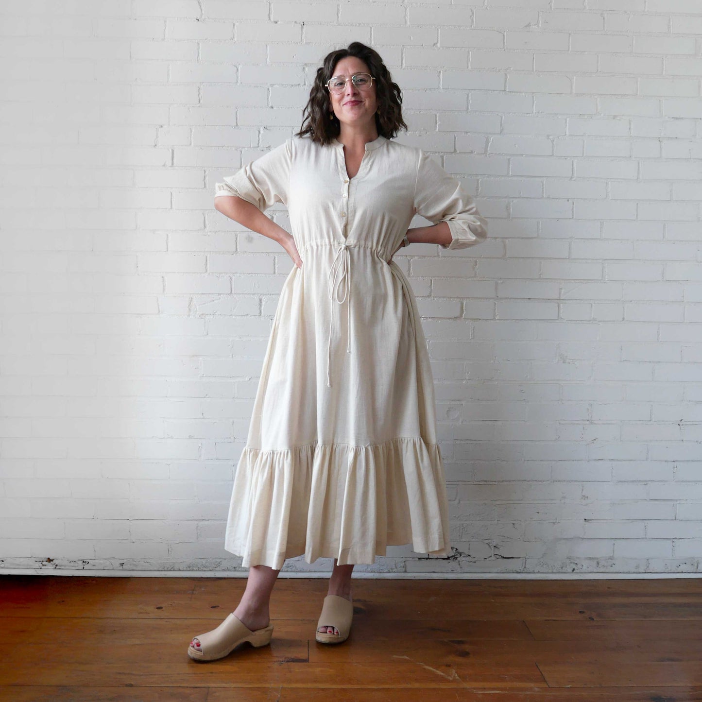 Woman wearing a white dress standing against a white brick wall.