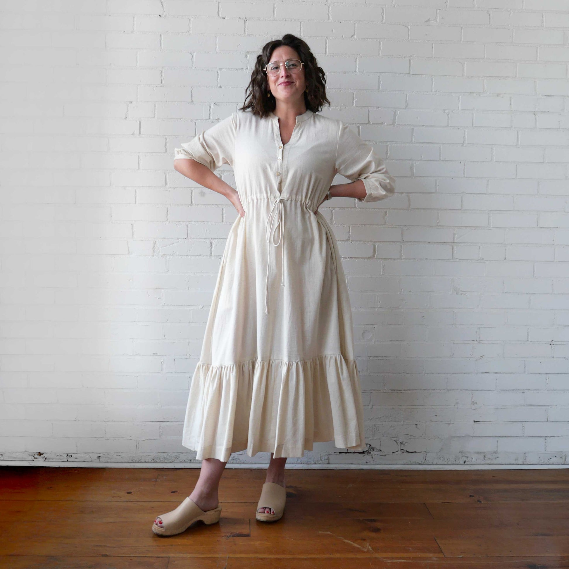 Woman wearing a white dress standing against a white brick wall.