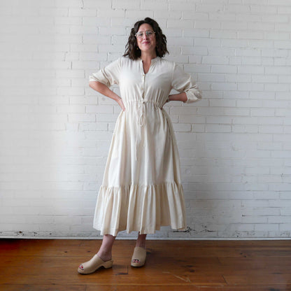 Woman wearing a white dress standing against a white brick wall.