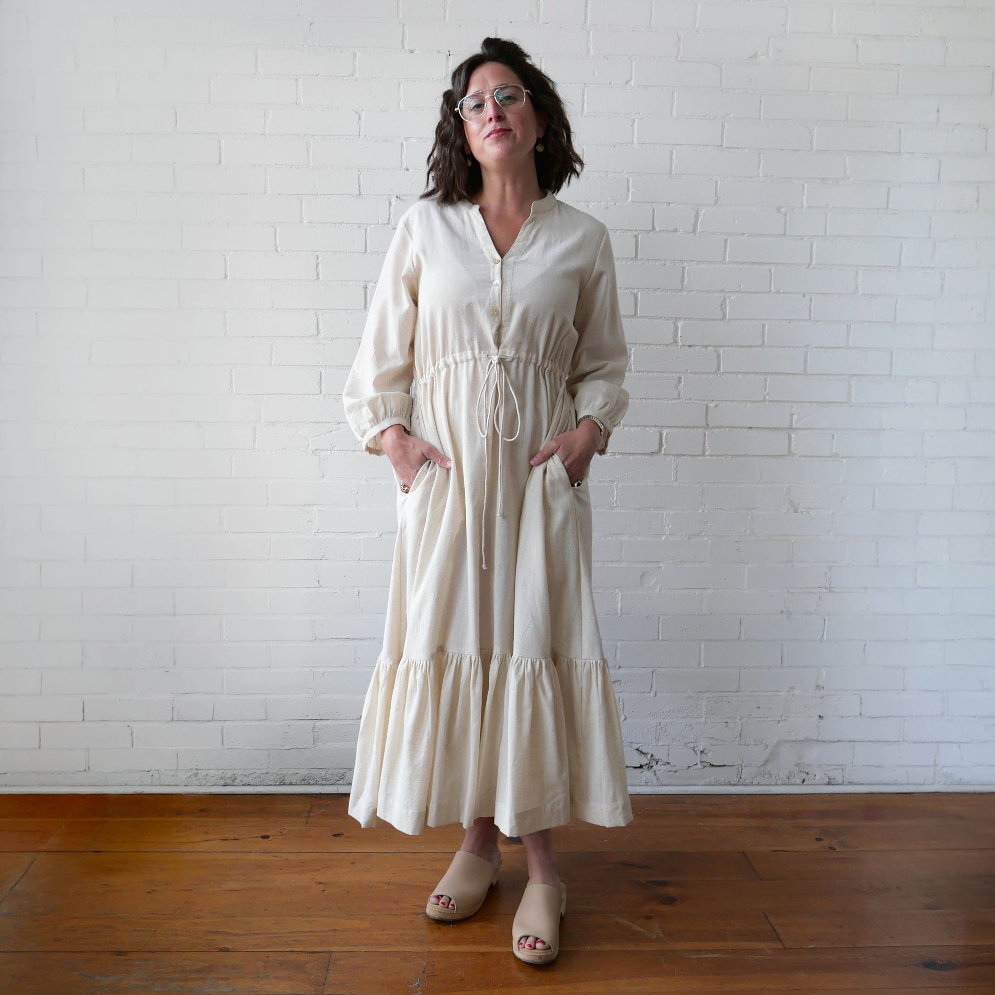 Woman wearing a white dress standing against a white brick wall.