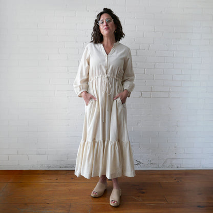 Woman wearing a white dress standing against a white brick wall.