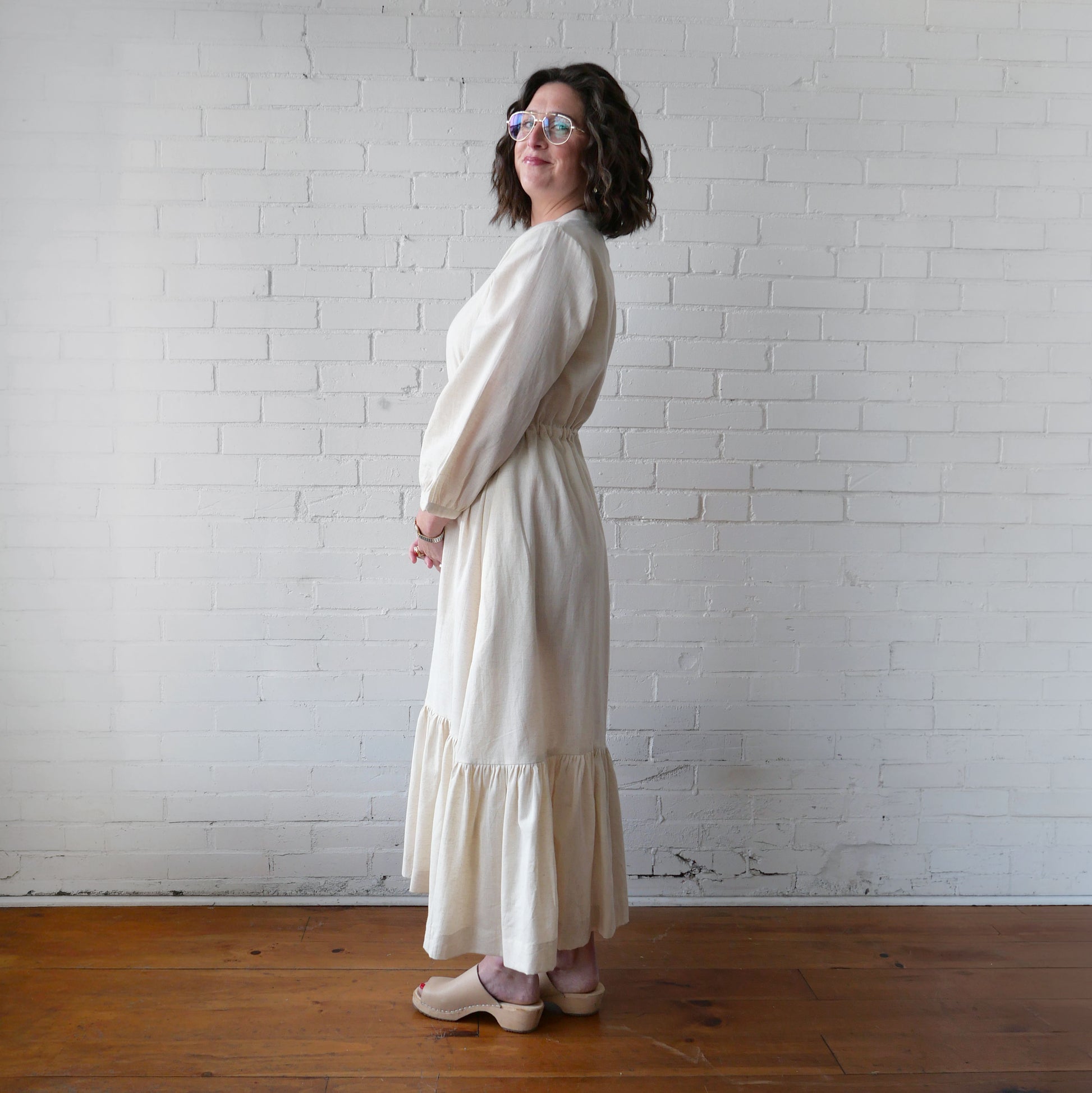 Woman wearing a long, light-colored dress against a white brick wall.