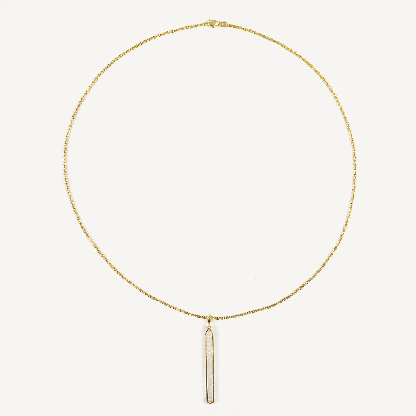 Gold necklace with a vertical bar pendant on a light beige background