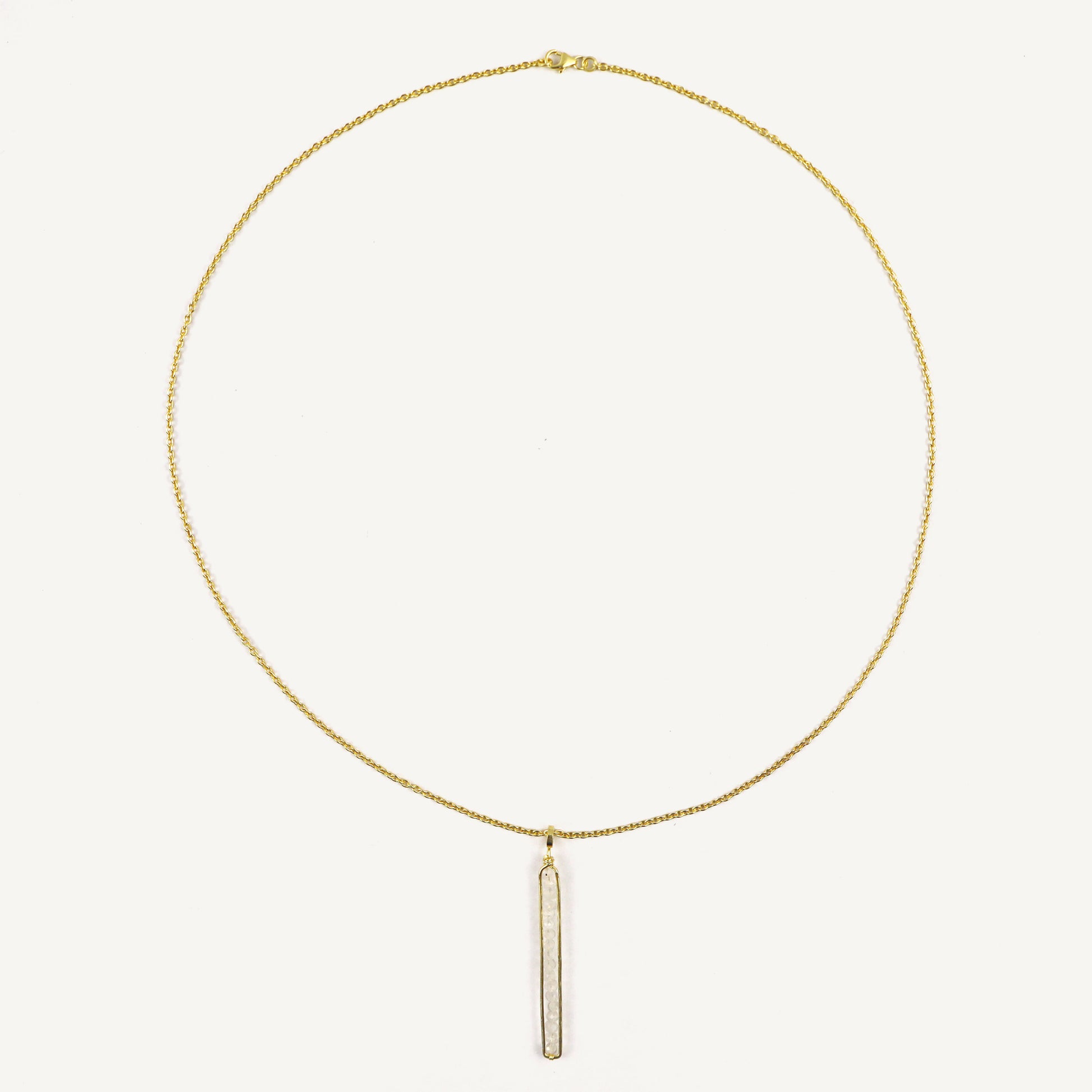 Gold necklace with a vertical bar pendant on a light beige background