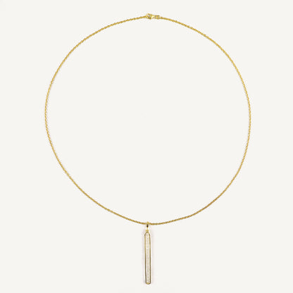 Gold necklace with a vertical bar pendant on a light beige background