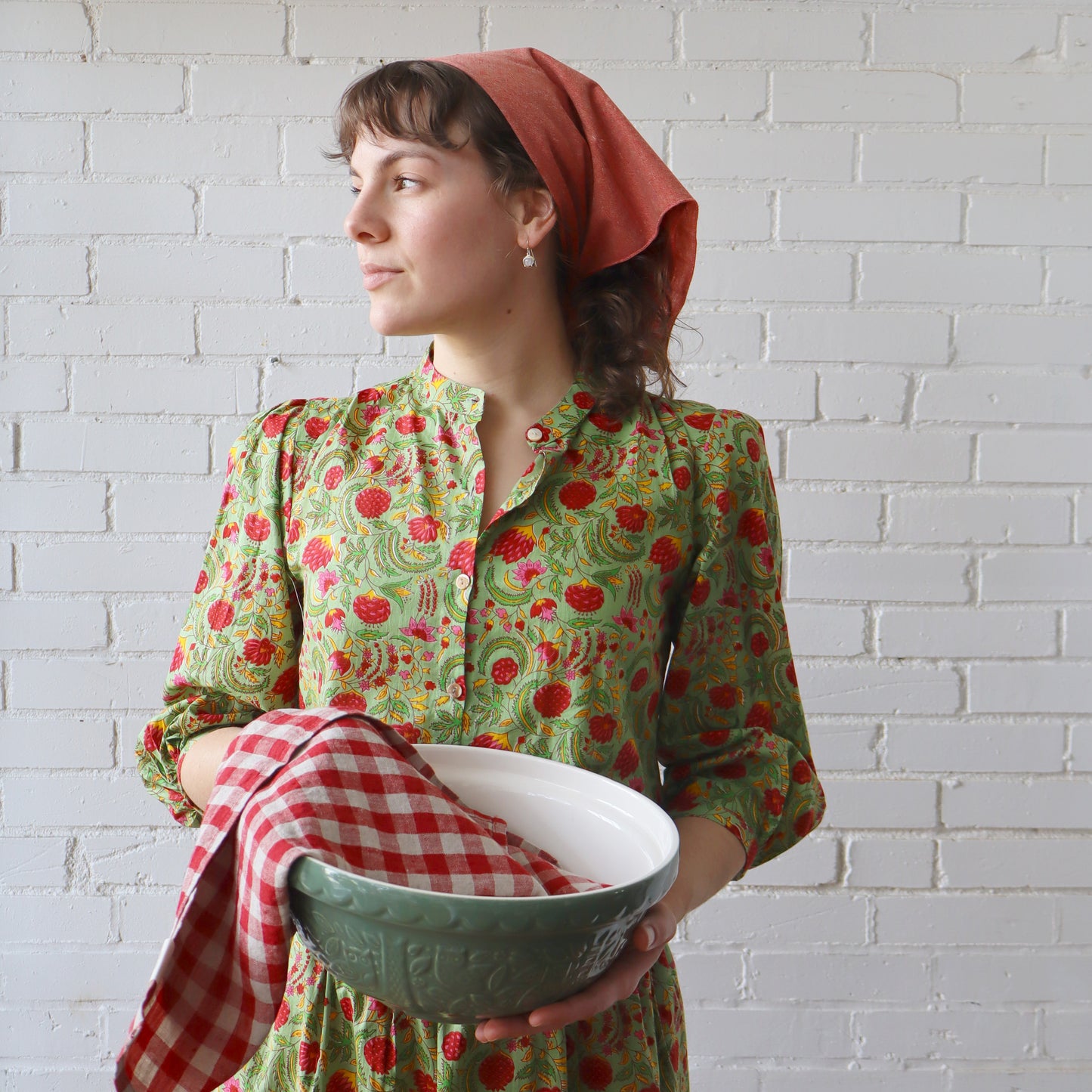 Woman in a floral dress holding a green bowl with a white brick wall background