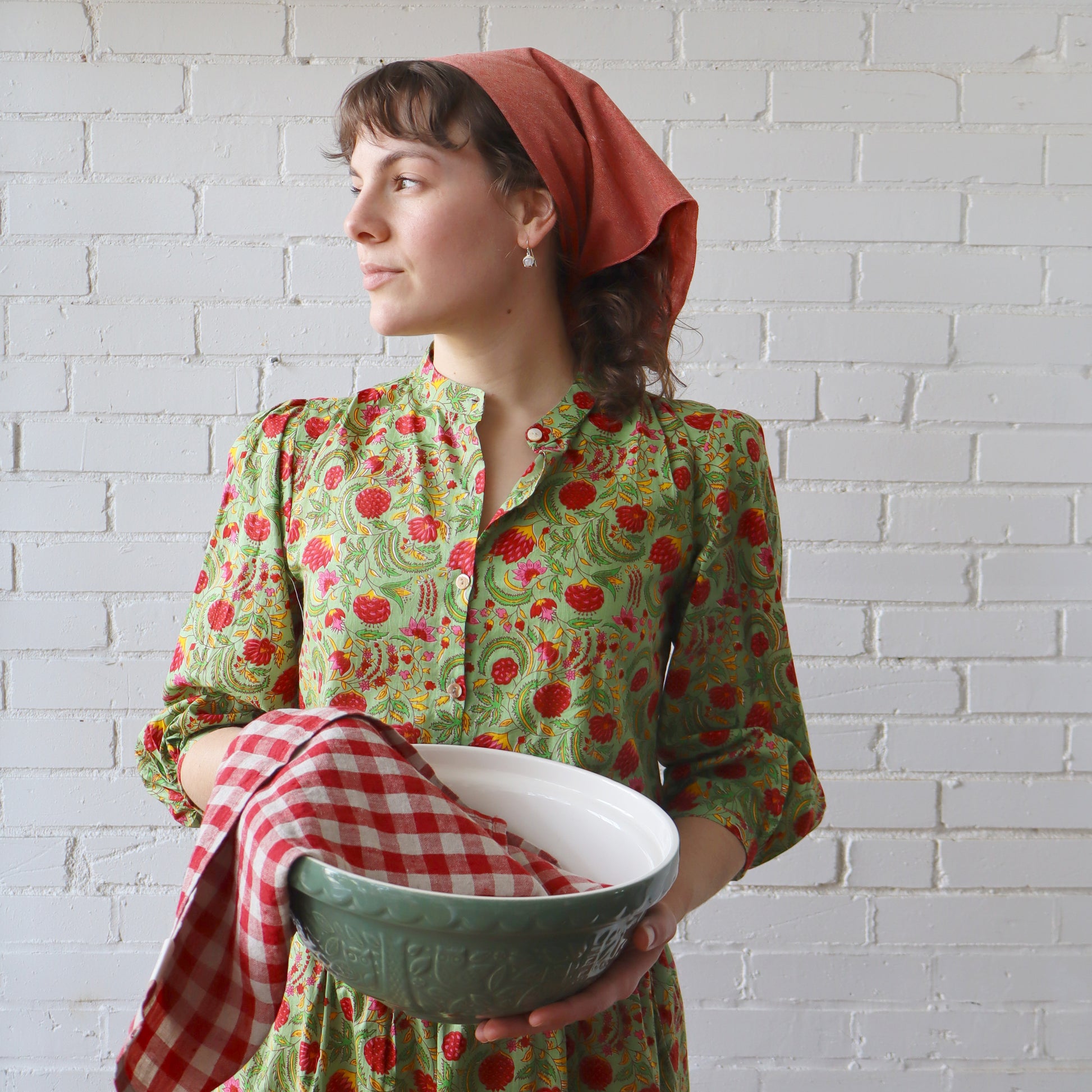 Woman in a floral dress holding a green bowl with a white brick wall background