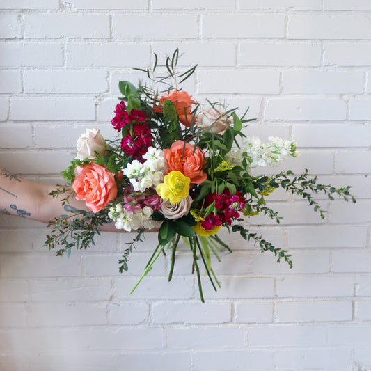 Bouquet of colorful flowers held against a white brick wall