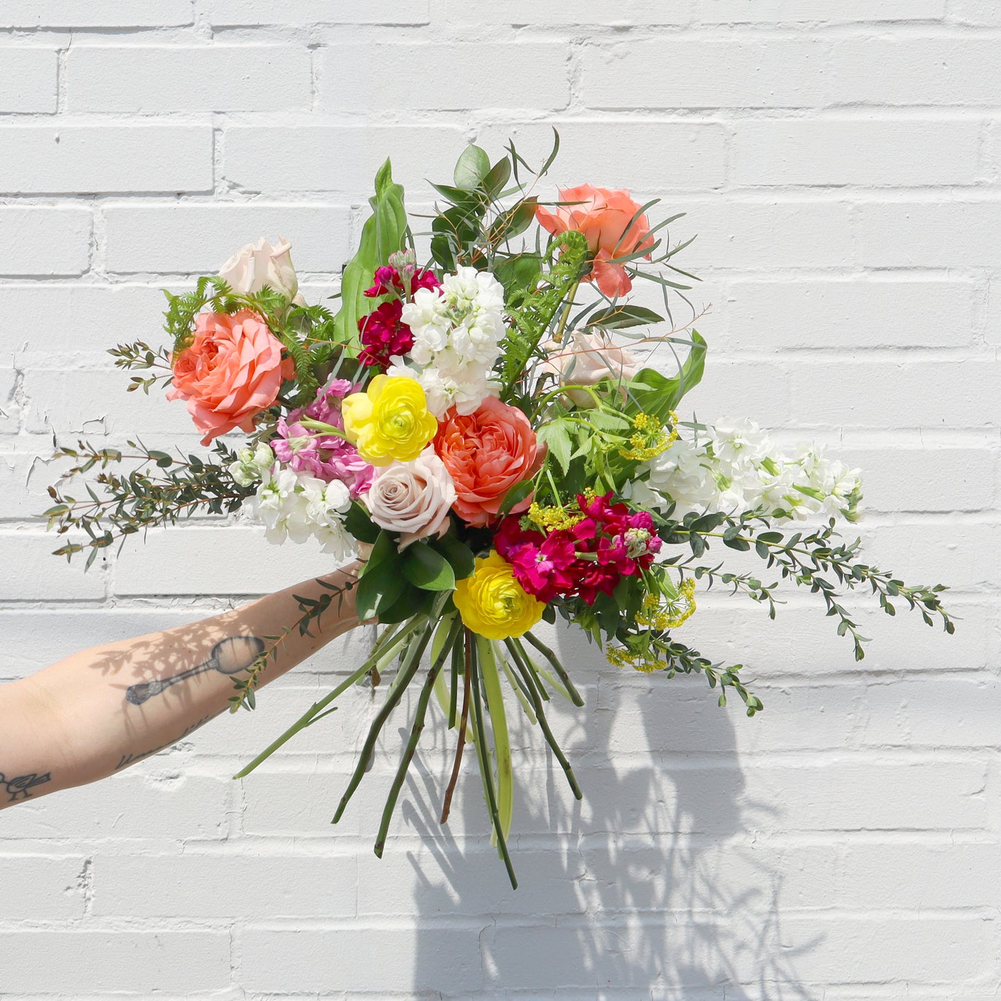 Bouquet of colorful flowers held against a white brick wall