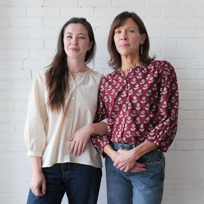 Two women standing side by side against a white brick wall.