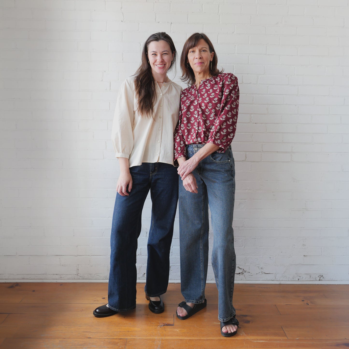 Two women standing together against a white brick wall.