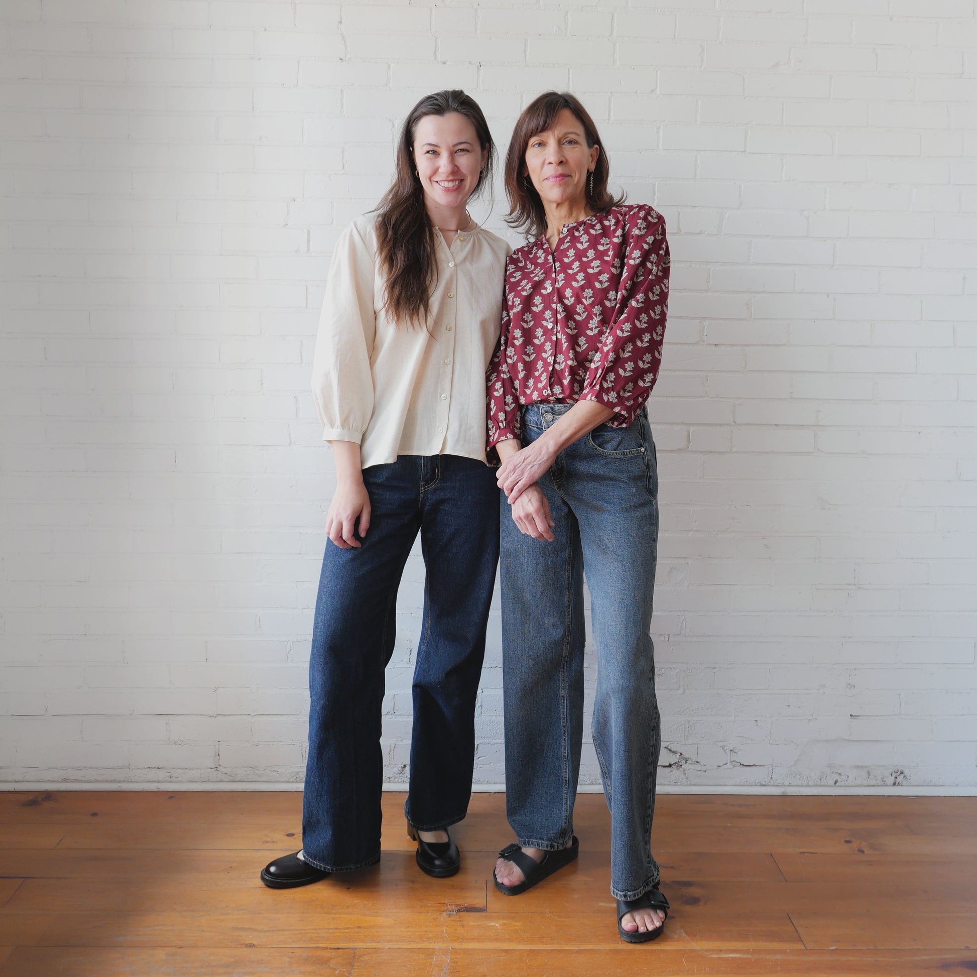 Two women standing together against a white brick wall.