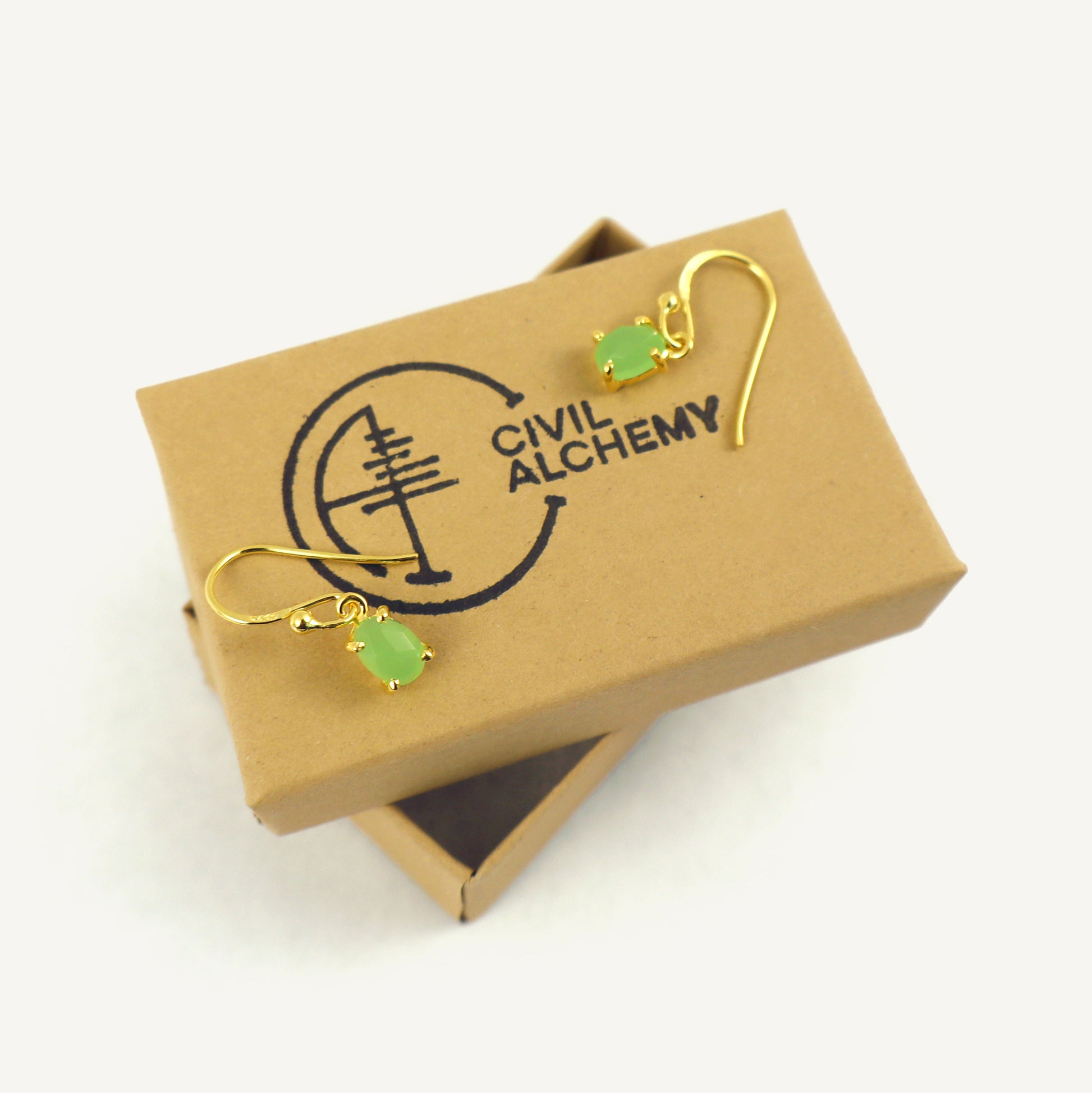 Gold earrings with green gemstones on a box labeled 'Civil Alchemy'.