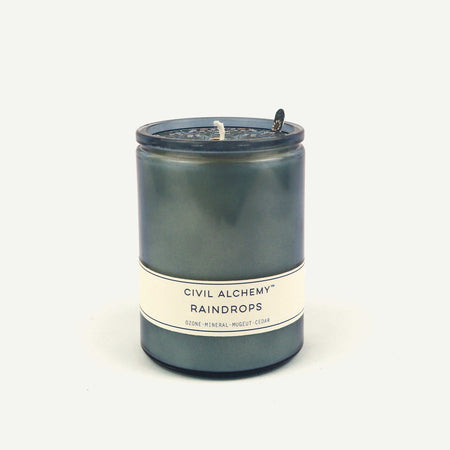 Candle with 'Civil Alchemy Raindrops' label on a white background