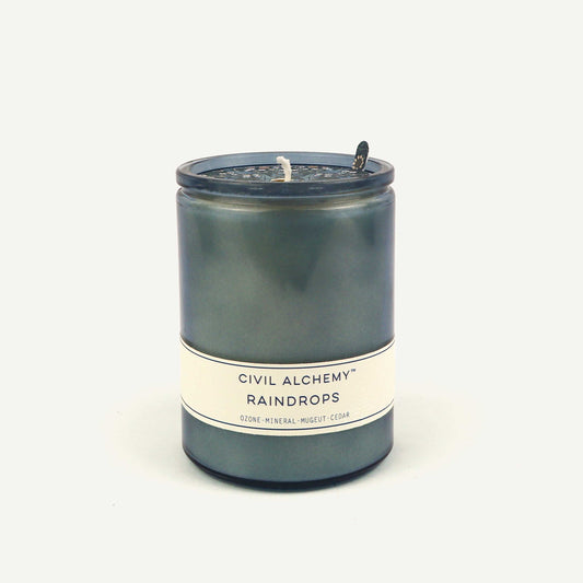 Candle with 'Civil Alchemy Raindrops' label on a white background