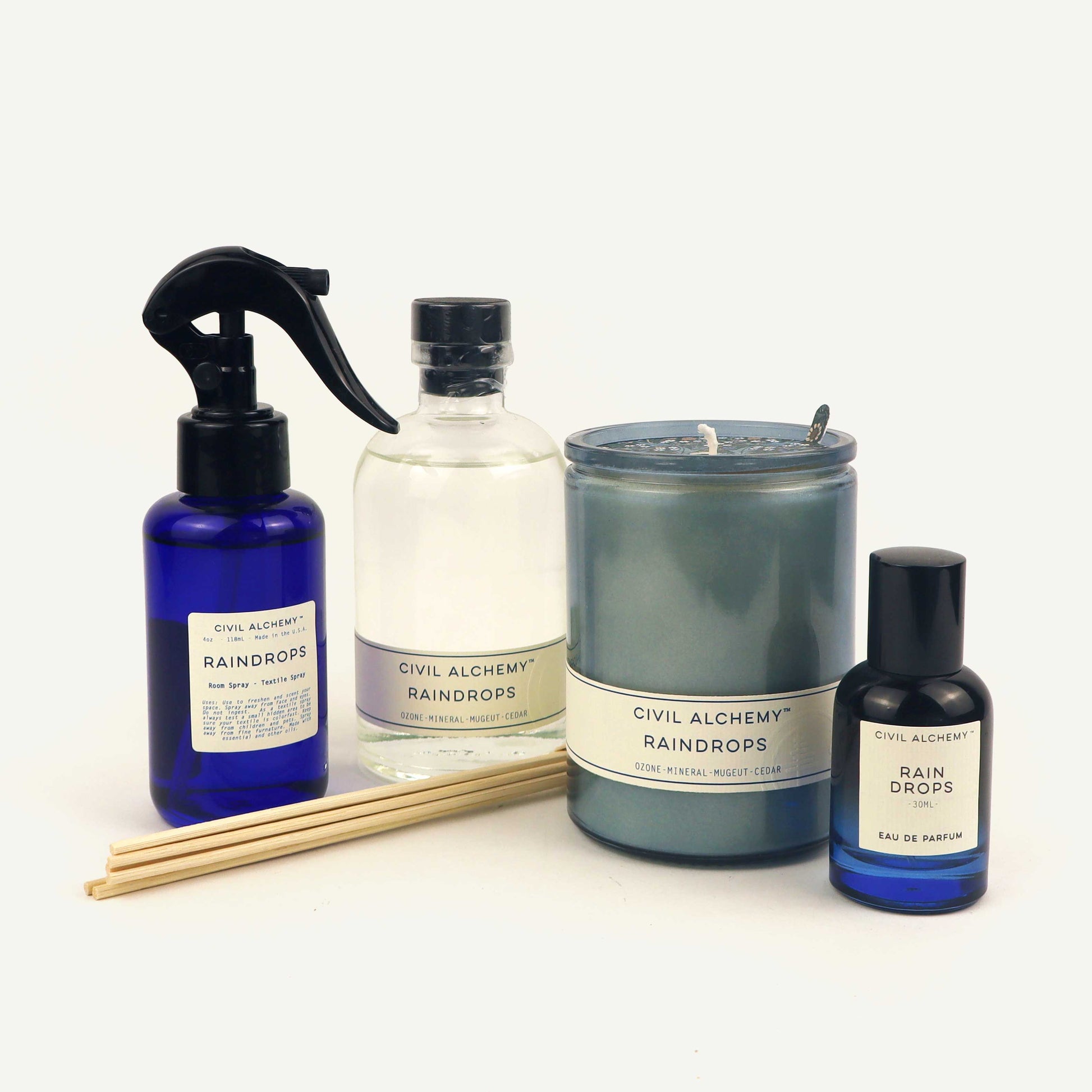 Collection of 'Civil Alchemy Raindrops' products including a spray bottle, diffuser, candle, and eau de parfum on a white background.