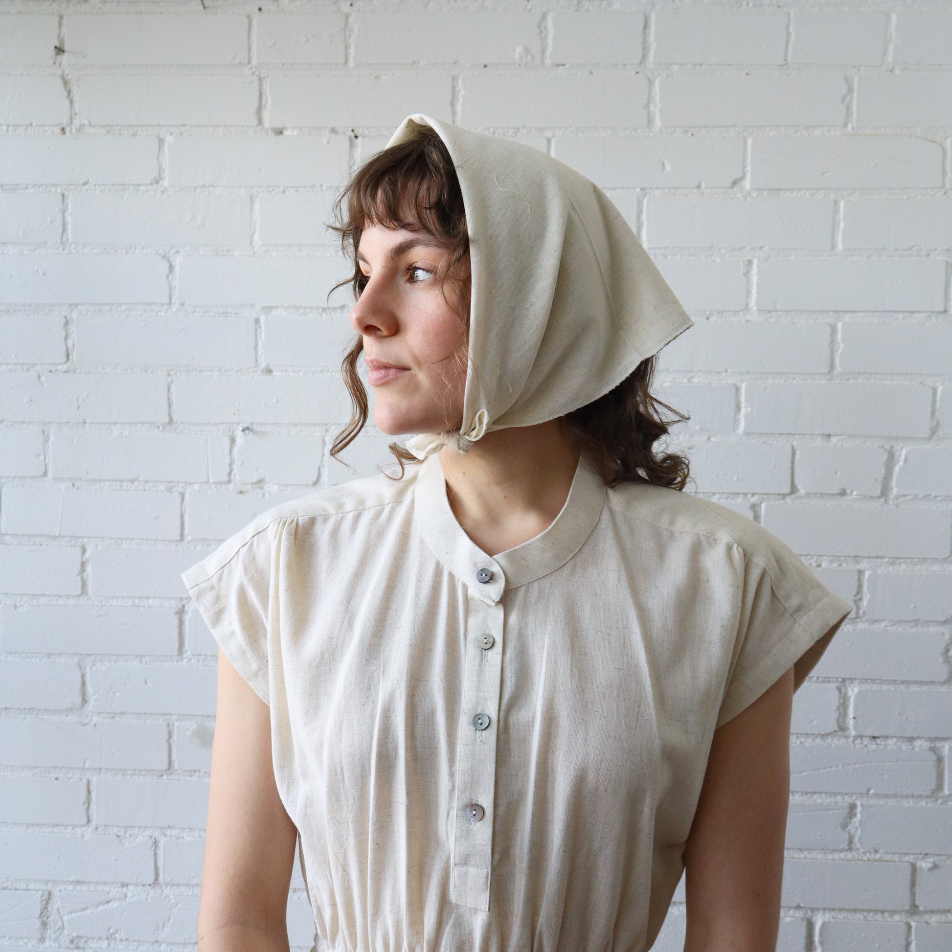Woman wearing a beige bonnet against a white brick wall