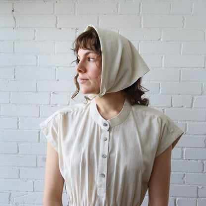 Woman wearing a beige bonnet against a white brick wall