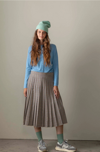Woman wearing a blue sweater, plaid skirt, and green beanie against a plain background