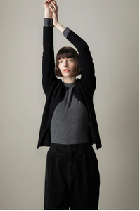 Person wearing a black jacket and gray shirt against a plain background