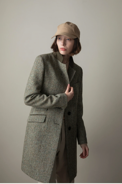 Person wearing a long green coat and beige cap against a plain background