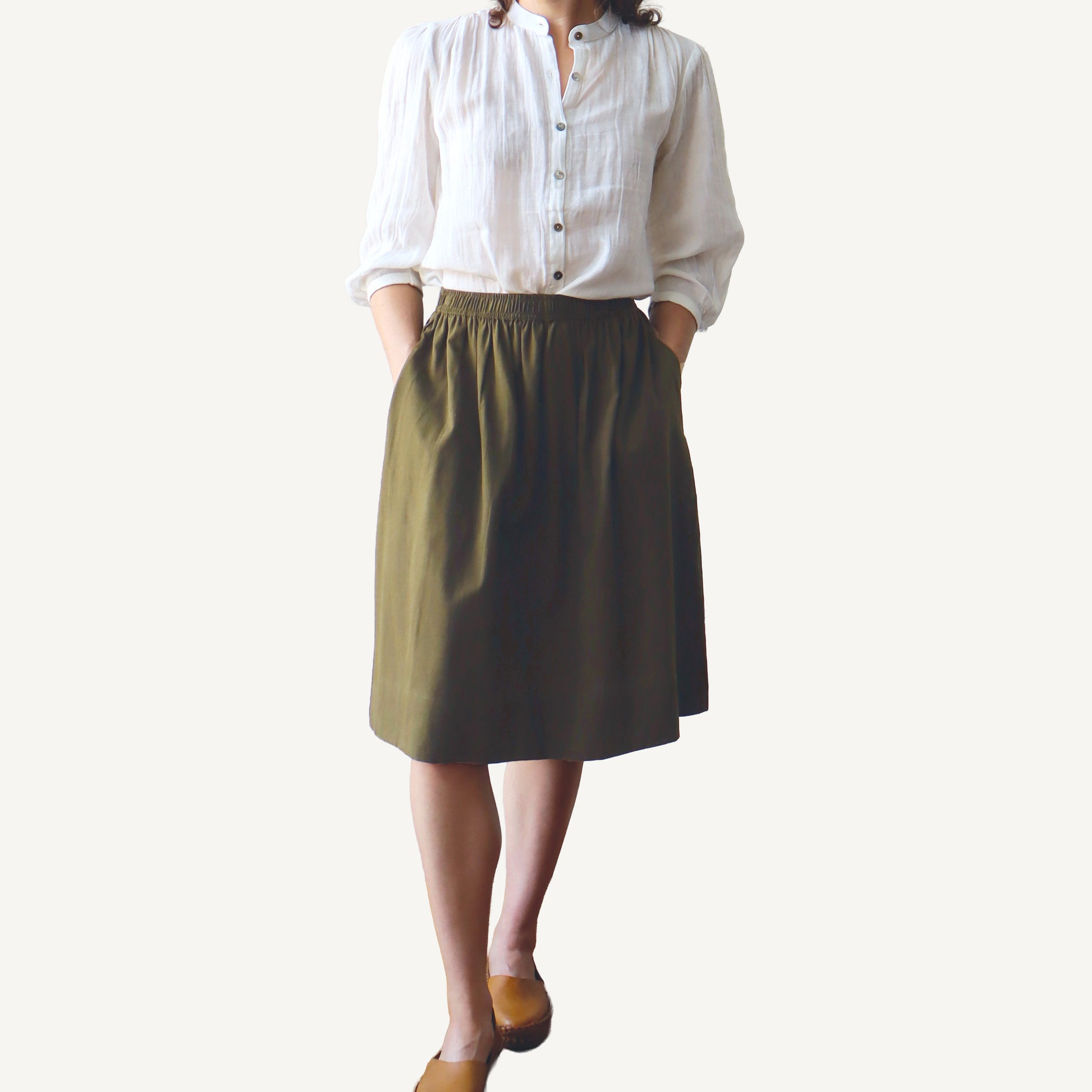 Person wearing a white shirt and olive green skirt on a plain background