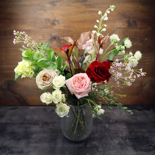 Bouquet of flowers in a clear vase on a dark surface with a wooden background