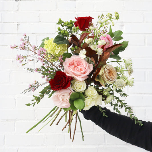 Bouquet of flowers held by a person against a white brick wall