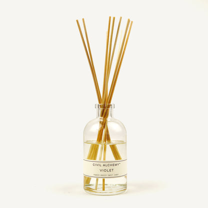 Clear glass diffuser bottle with wooden sticks labeled 'Violet' by Civil Alchemy on a white background