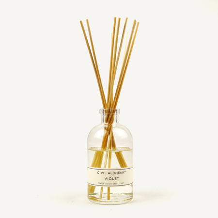 Clear glass diffuser bottle with wooden sticks labeled 'Violet' by Civil Alchemy on a white background