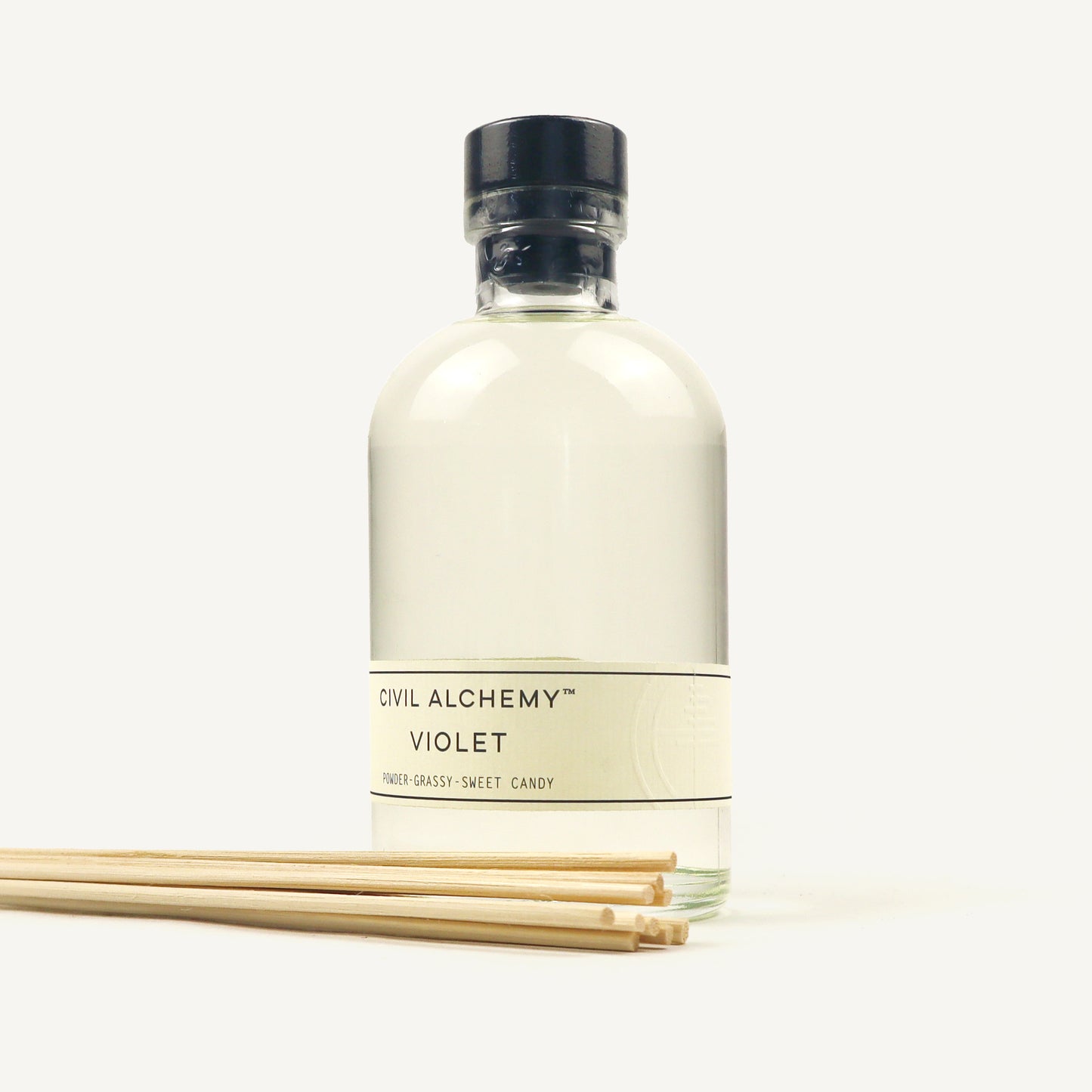 Bottle of Civil Alchemy Violet fragrance with reed diffuser sticks on a white background