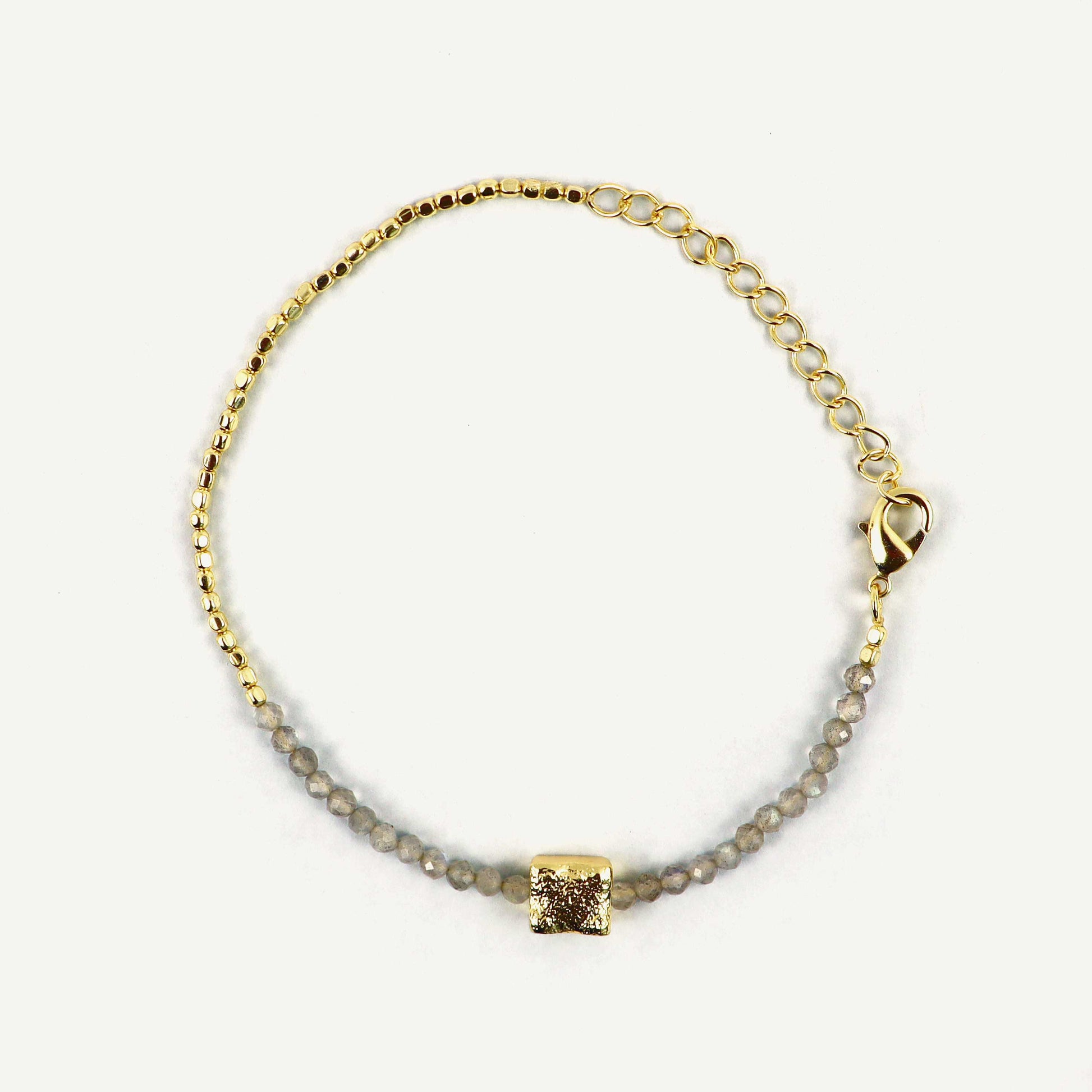 Gold bracelet with a square pendant on a light gray background