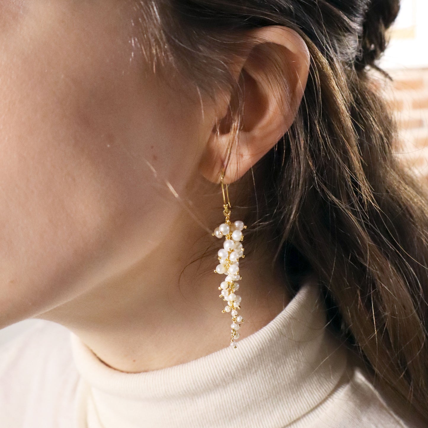 Close-up of a person wearing a delicate gold earring with pearls.
