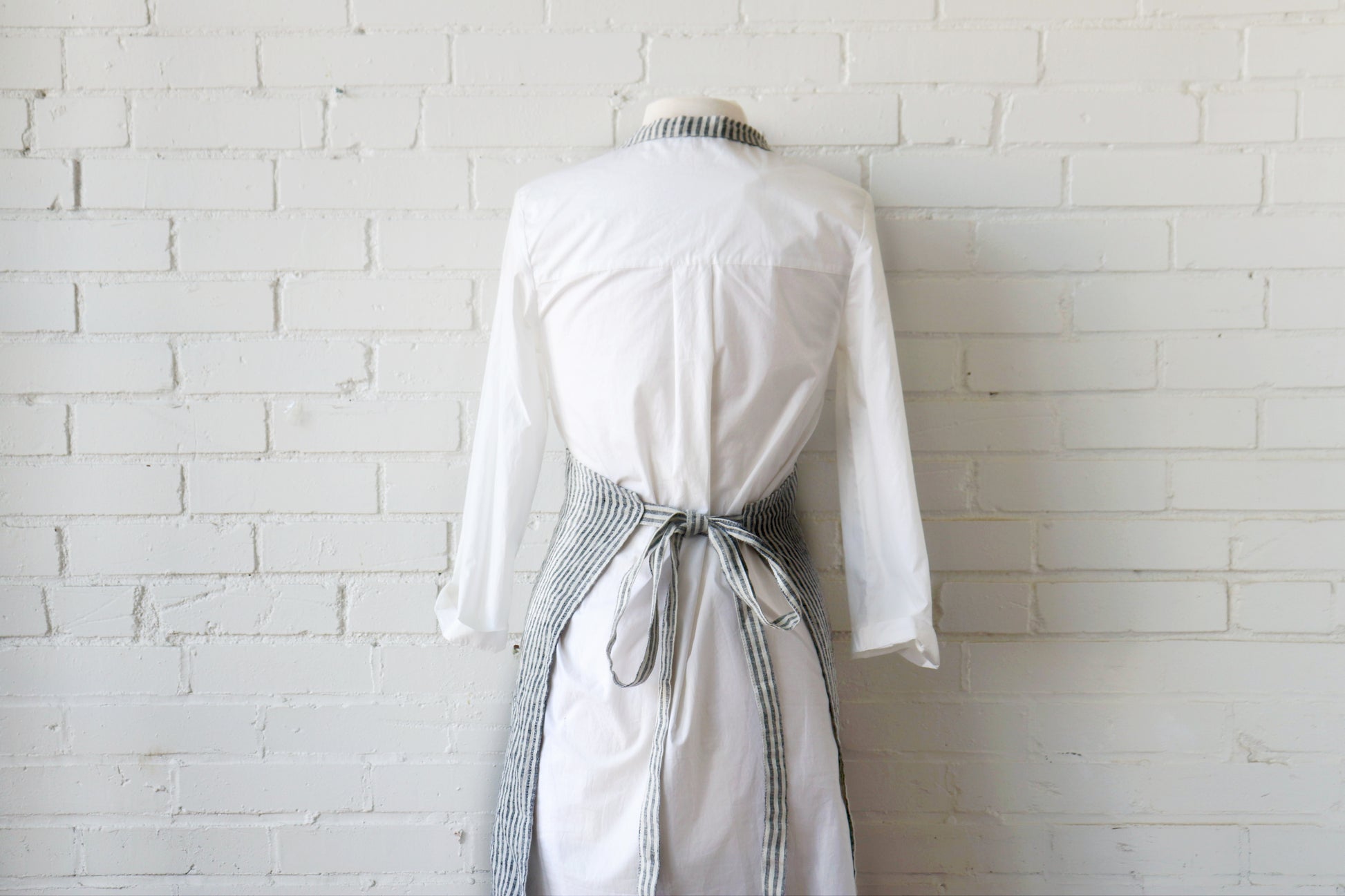 White dress with a belt on a mannequin against a white brick wall