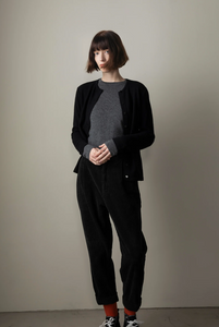 Person wearing a black outfit with a gray sweater against a plain background
